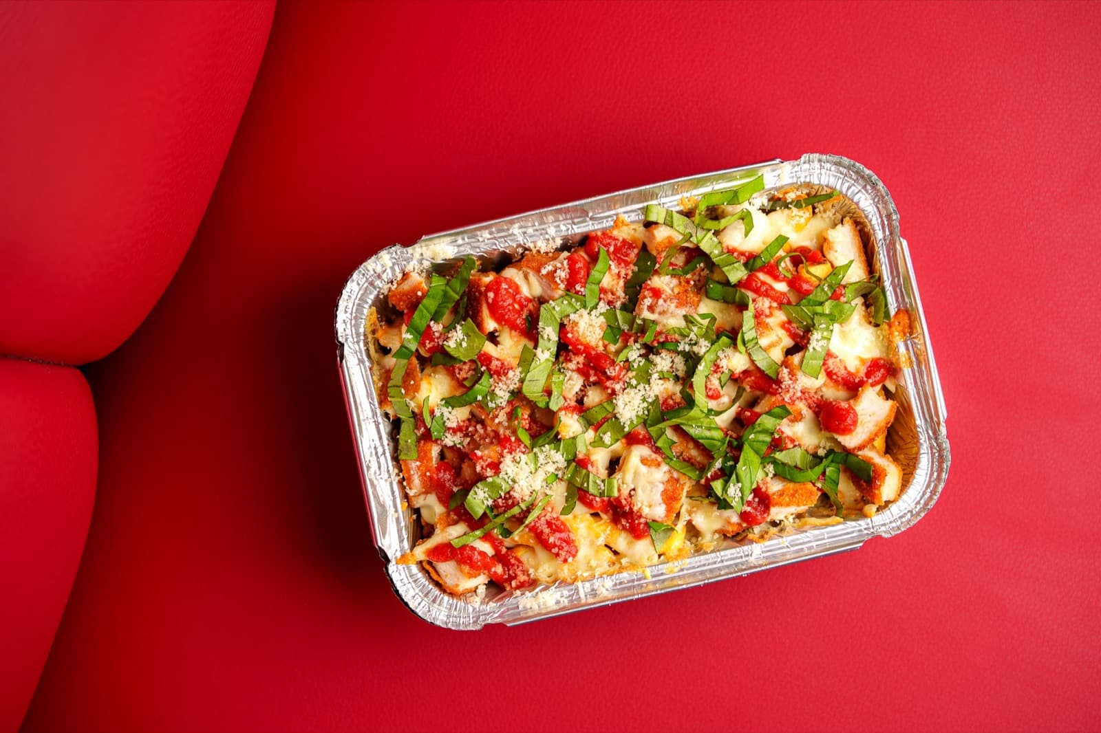 Barquette de poulet parmesan gratiné, sauce tomate et basilic frais, sur banquette rouge